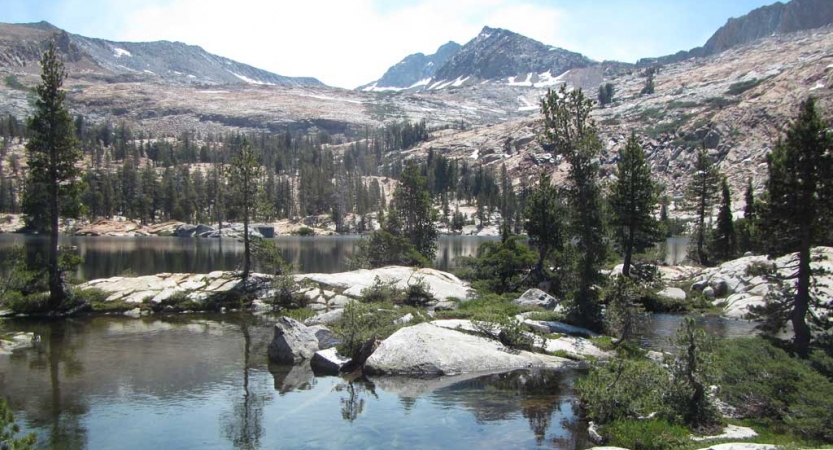 An alpine lake is dotted with boulders and evergreen trees.